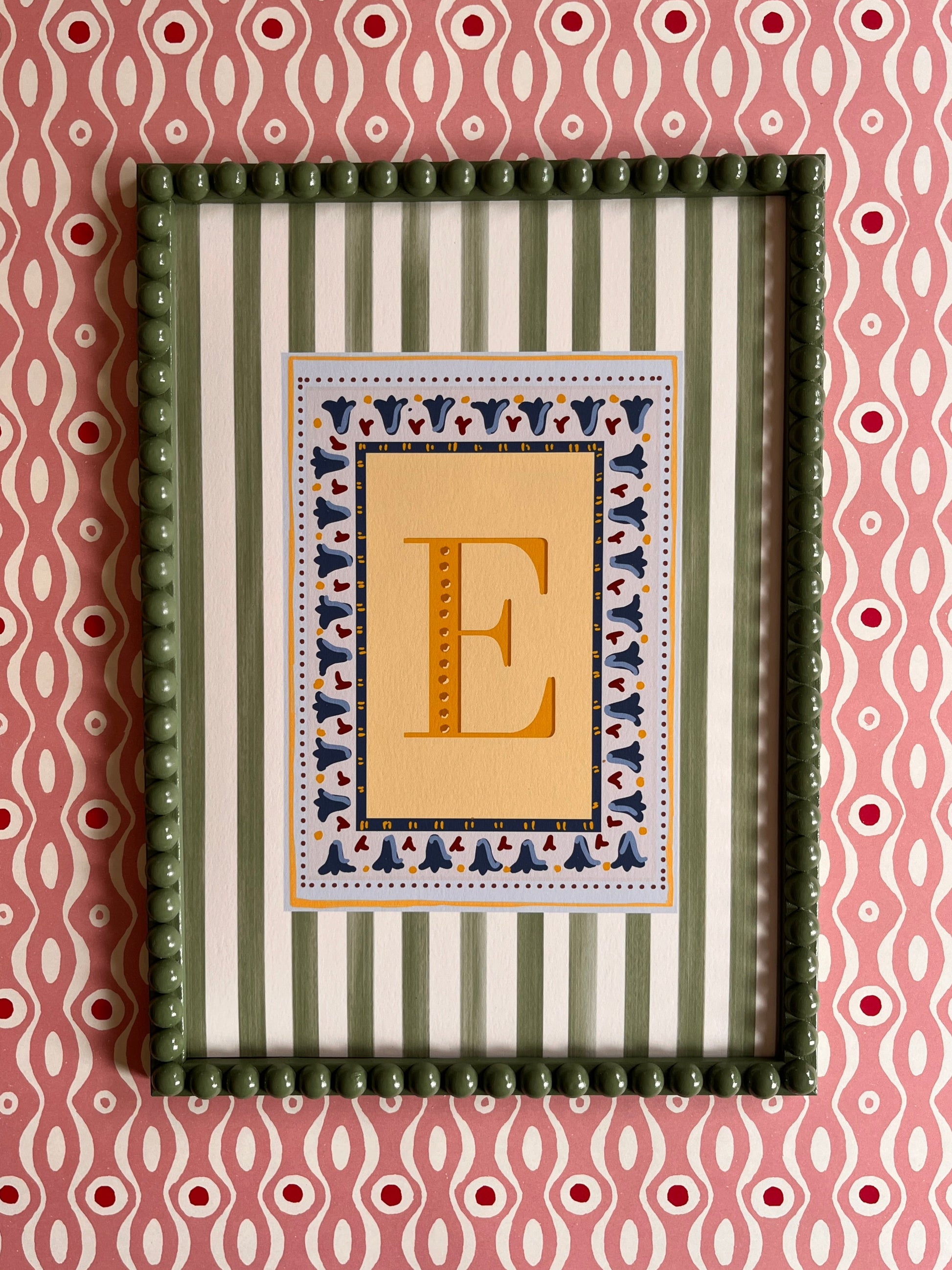 Decorative framed alphabet artwork with the letter E in yellow surrounded geometric green and white striped pattern border on a pink and white background