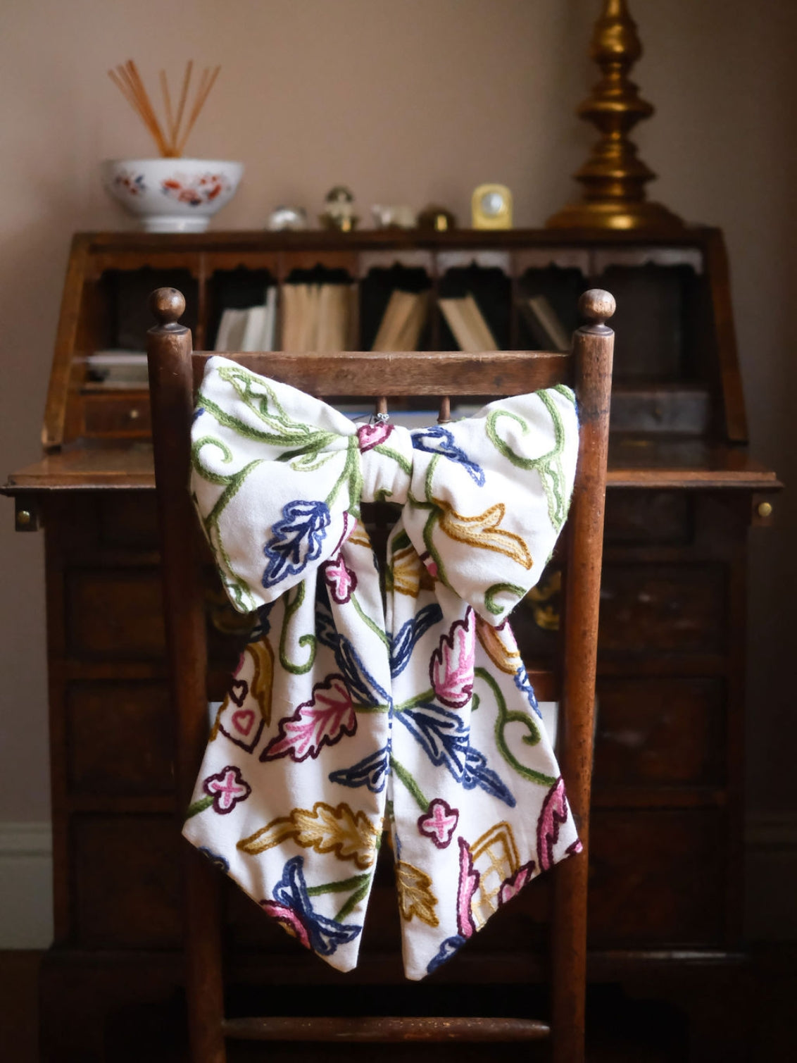 Hand-embroidered vintage fabric crewel work bow with vibrant floral and vine motifs in pink green, blue, and ochre, styled in a traditional countryside cotswold home — perfect as a decorative accent for furniture,  door knobs, the garden or seasonal home styling, it would also make a unique gift 