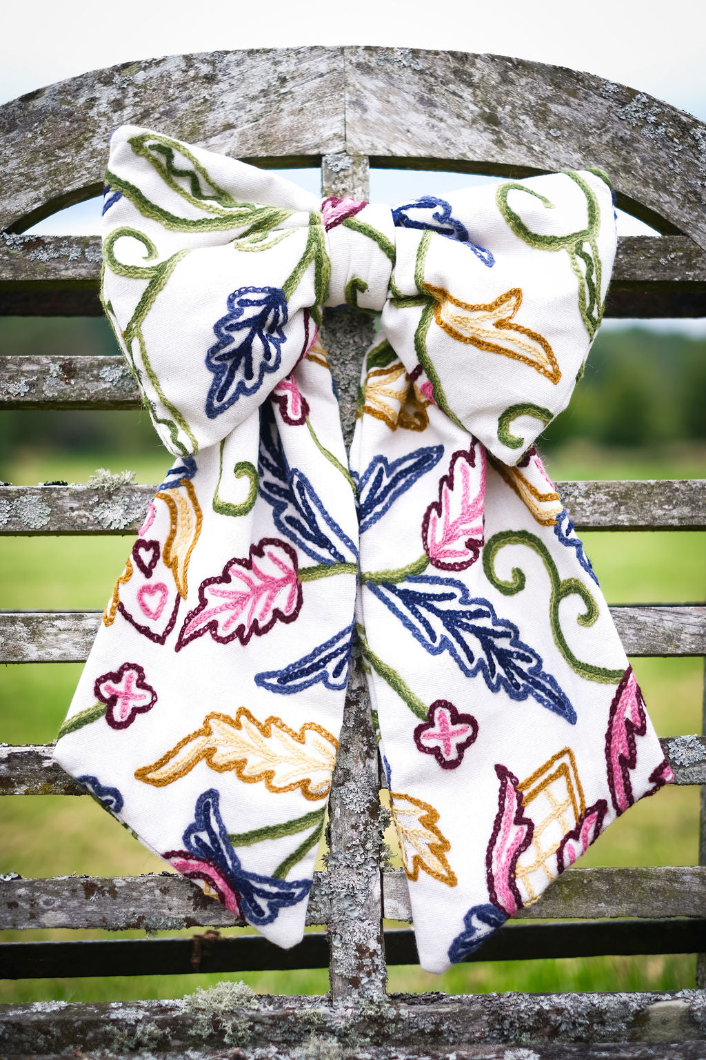 Hand-embroidered vintage fabric crewel work bow with vibrant floral and vine motifs in pink, green, blue, and ochre, styled in a traditional countryside cotswold home — perfect as a decorative accent for furniture,  door knobs, the garden or seasonal home styling, it would also make a unique gift 