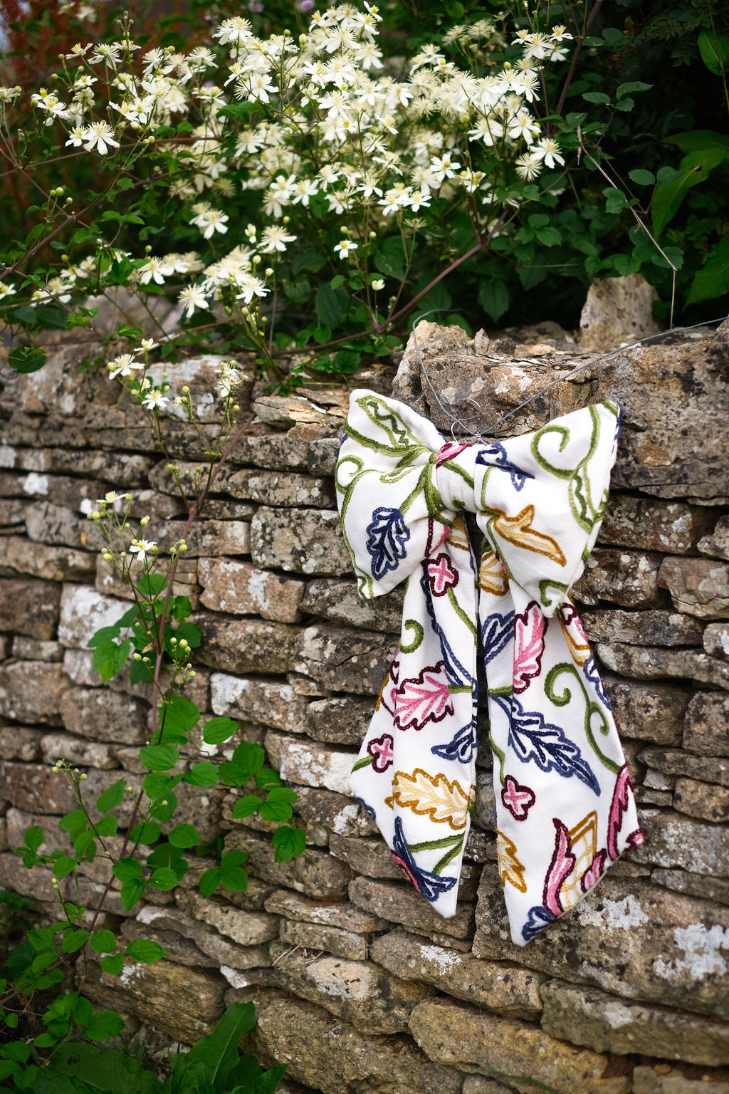 Hand-embroidered vintage fabric crewel work bow with vibrant floral and vine motifs in pink, green, blue, and ochre, styled in a traditional countryside cotswold home — perfect as a decorative accent for furniture,  door knobs, the garden or seasonal home styling, it would also make a unique gift 