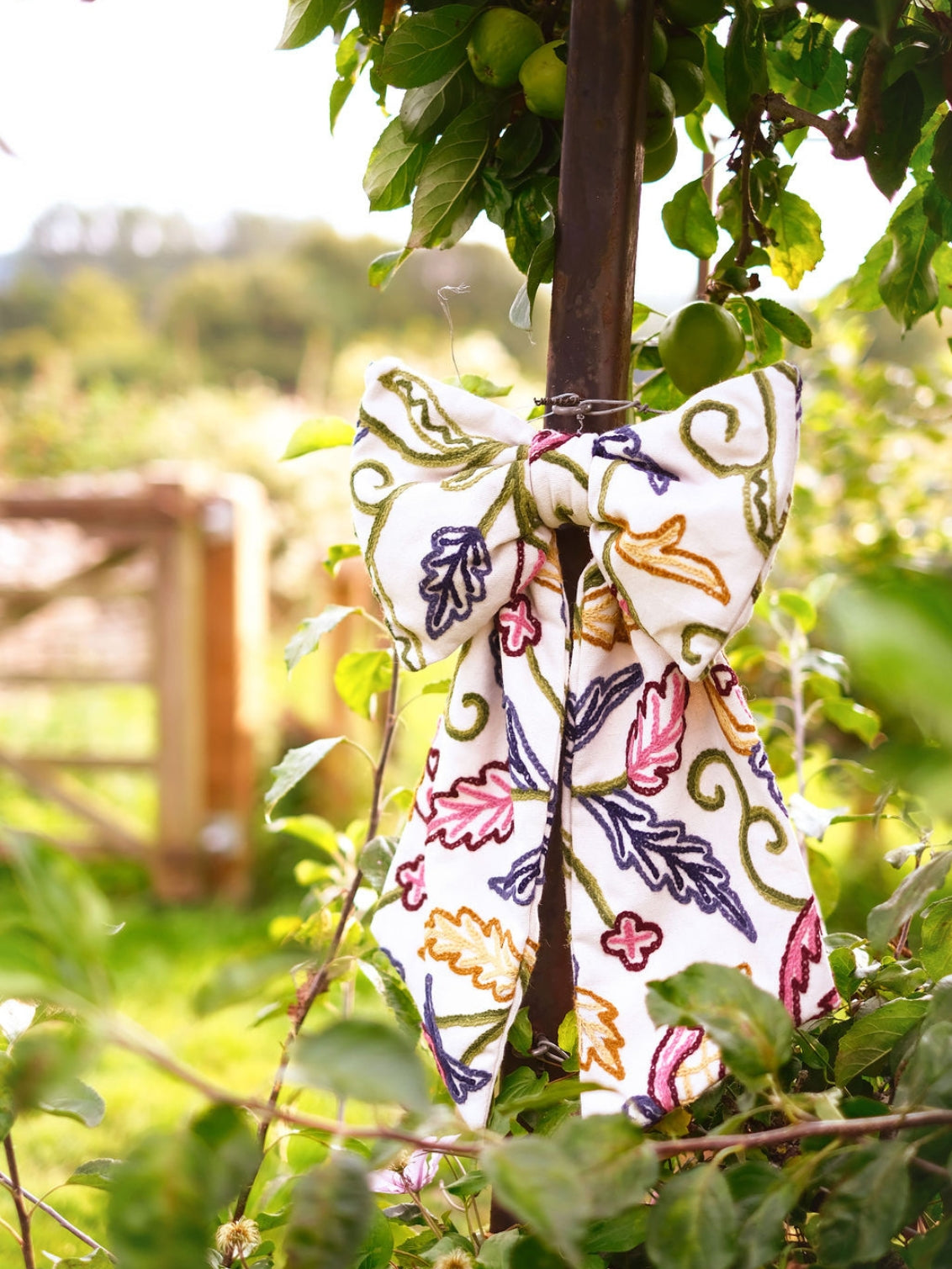 Hand-embroidered vintage fabric crewel work bow with vibrant floral and vine motifs in pink, green, blue, and ochre, styled in a traditional countryside cotswold home — perfect as a decorative accent for furniture,  door knobs, the garden or seasonal home styling, it would also make a unique gift 