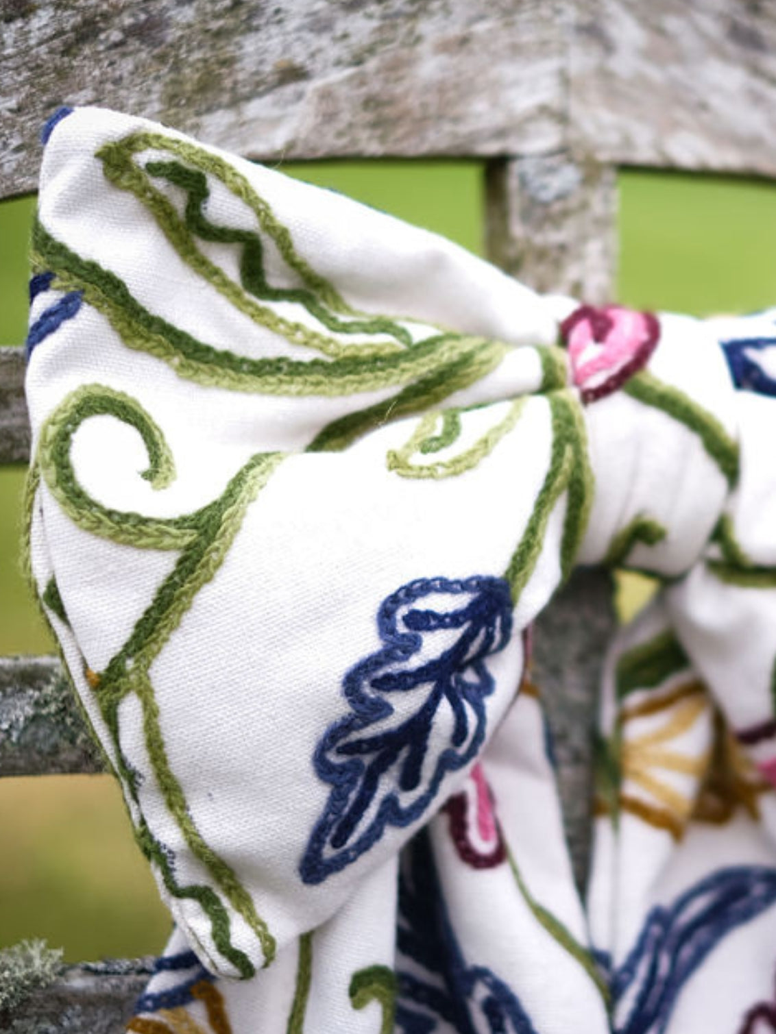 Detail photo of Hand-embroidered vintage fabric crewel work bow with vibrant floral and vine motifs in red, green, blue, and ochre, styled in a traditional countryside cotswold home — perfect as a decorative accent for furniture,  door knobs, the garden or seasonal home styling, it would also make a unique gift 