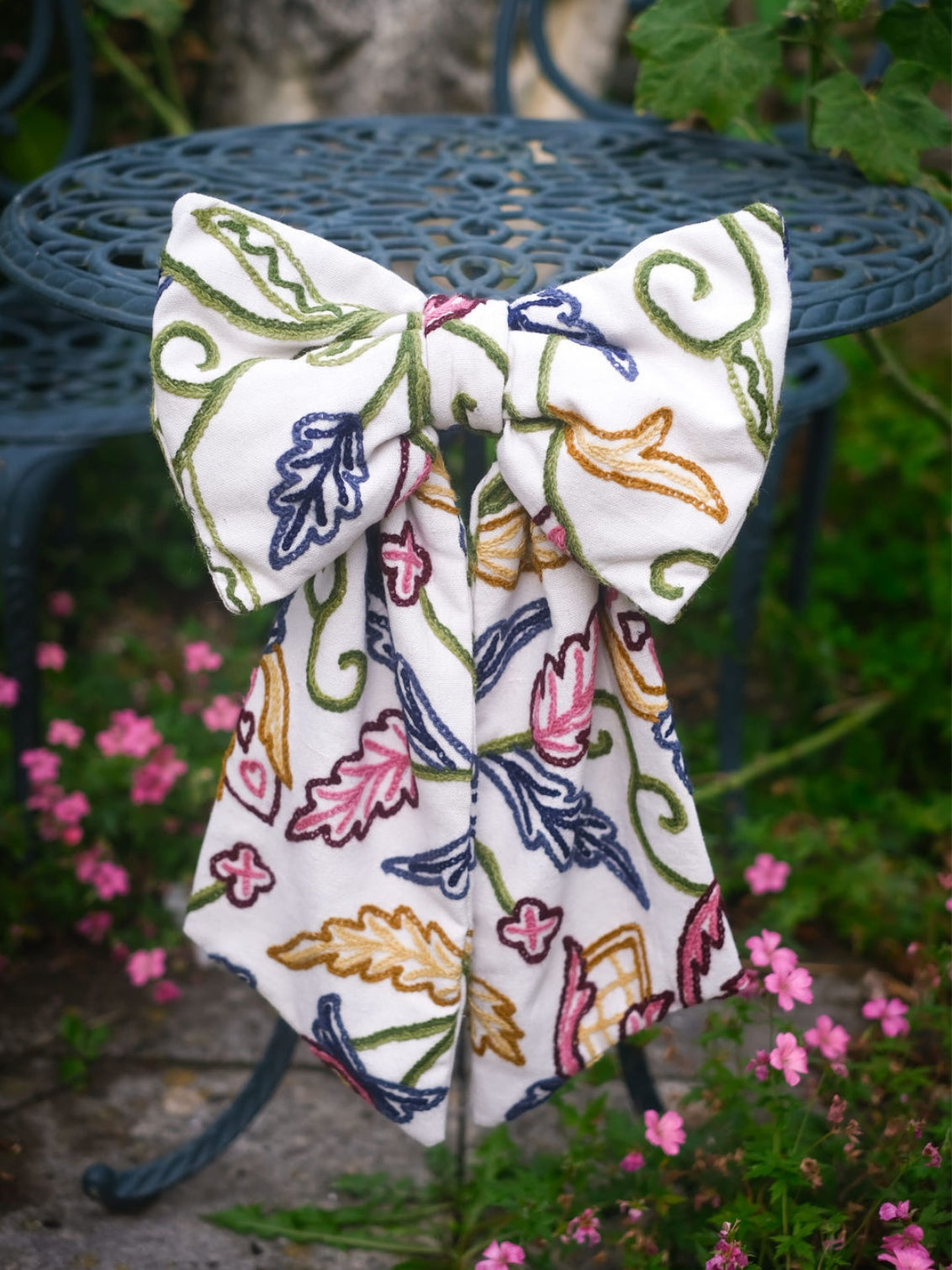 Hand-embroidered vintage fabric crewel work bow with vibrant floral and vine motifs in pink, green, blue, and ochre, styled in a traditional countryside cotswold home — perfect as a decorative accent for furniture,  door knobs, the garden or seasonal home styling, it would also make a unique gift 