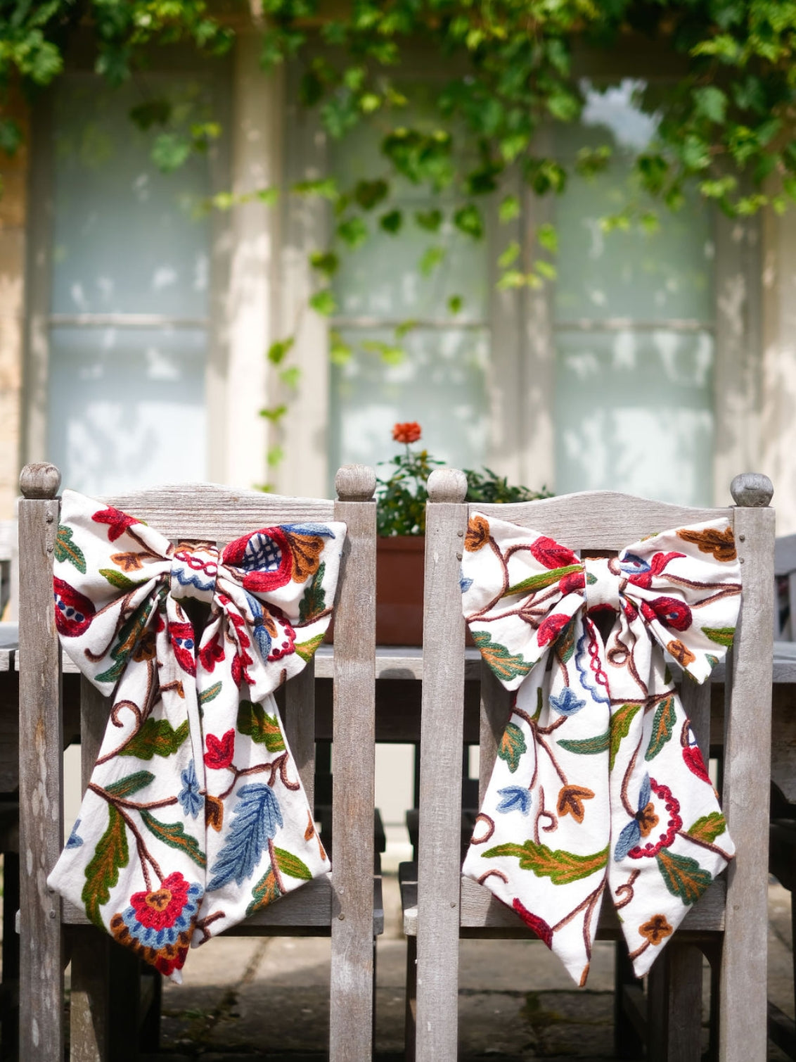 Hand-embroidered vintage fabric crewel work bow with vibrant floral and vine motifs in red, green, blue, and ochre, styled in a traditional countryside cotswold home — perfect as a decorative accent for furniture,  door knobs, the garden or seasonal home styling, it would also make a unique gift 