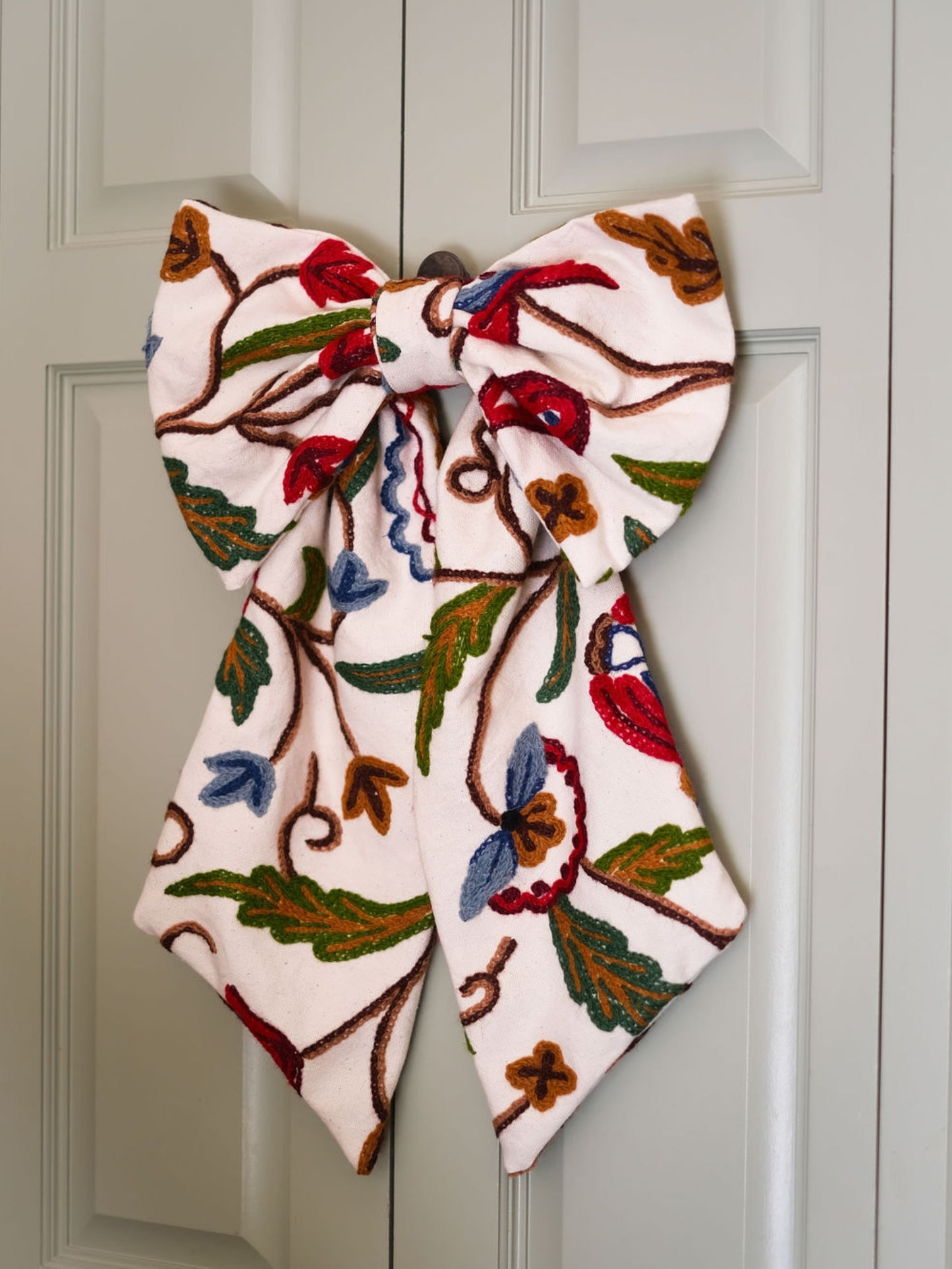 Hand-embroidered vintage fabric crewel work bow with vibrant floral and vine motifs in red, green, blue, and ochre, styled in a traditional countryside cotswold home — perfect as a decorative accent for furniture,  door knobs, the garden or seasonal home styling, it would also make a unique gift 