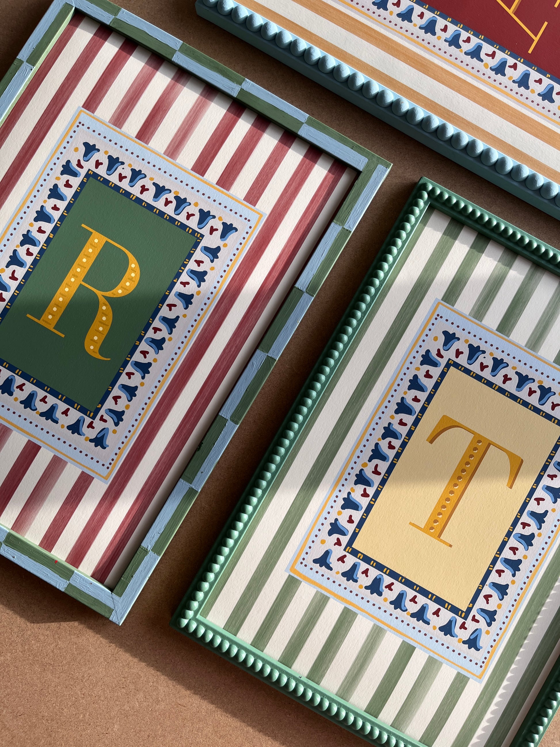 Decorative and unique alphabet wall art featuring your chosen letter in a bold muted colours, framed with a floral block-print style border and set against vertical muted stripes in contrast colours—ideal for playful nursery decor, alphabet print collections, and unique gift ideas for children’s playrooms and nursery decor as well as design lovers