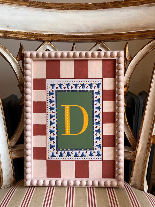 Decorative striped picture mounts in earthy muted tones framing an alphabet print, finished with a hand painted bobbin frame—ideal for enhancing botanical art prints and adding a unique, handcrafted touch to home decor or gift presentations