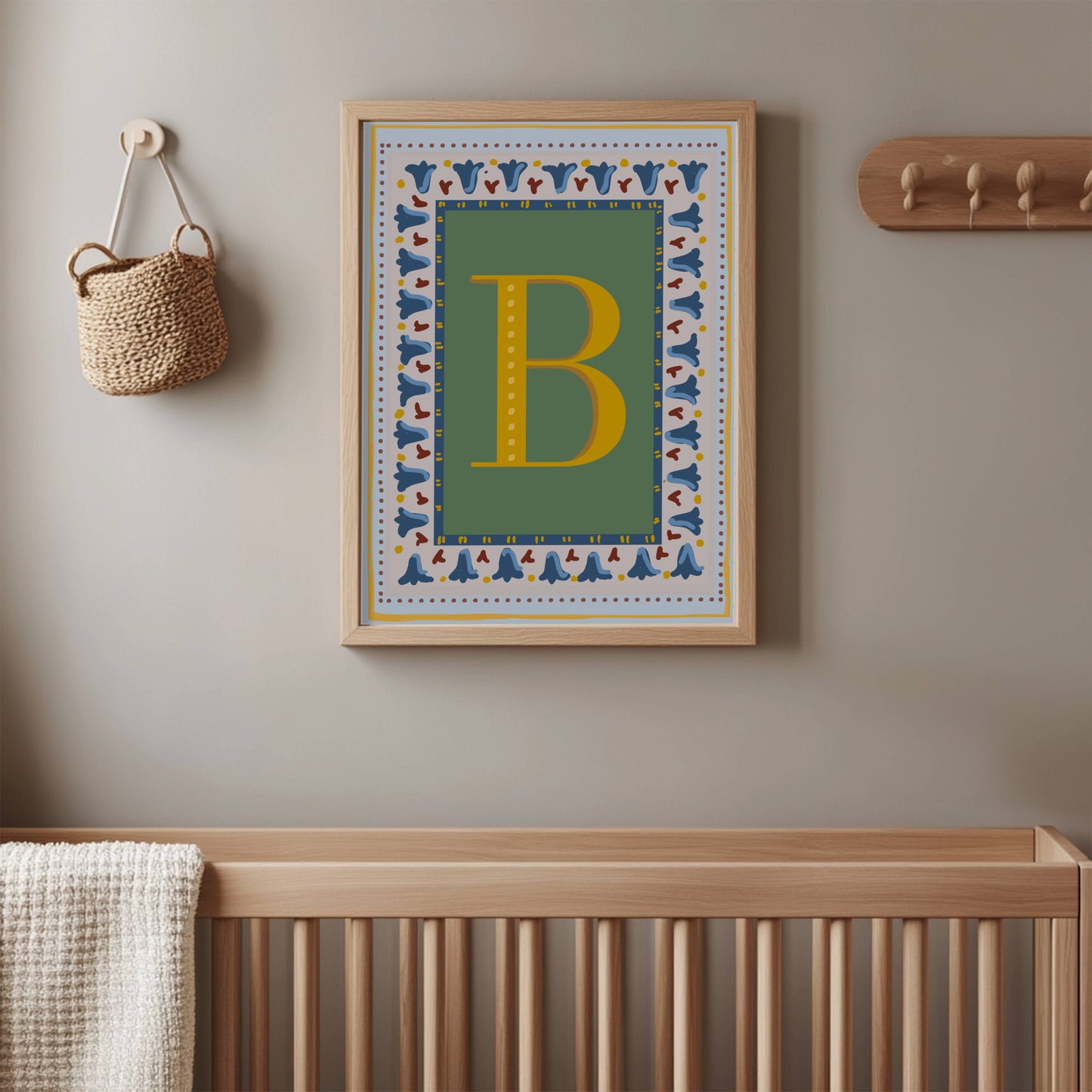 Personalised vintage initial letter print featuring a mustard yellow alphabet letter on a muted sage green background with blue floral border and dusty red striped detailing, styled in a light wooden bobbin frame for a gender-neutral nursery or children's bedroom.